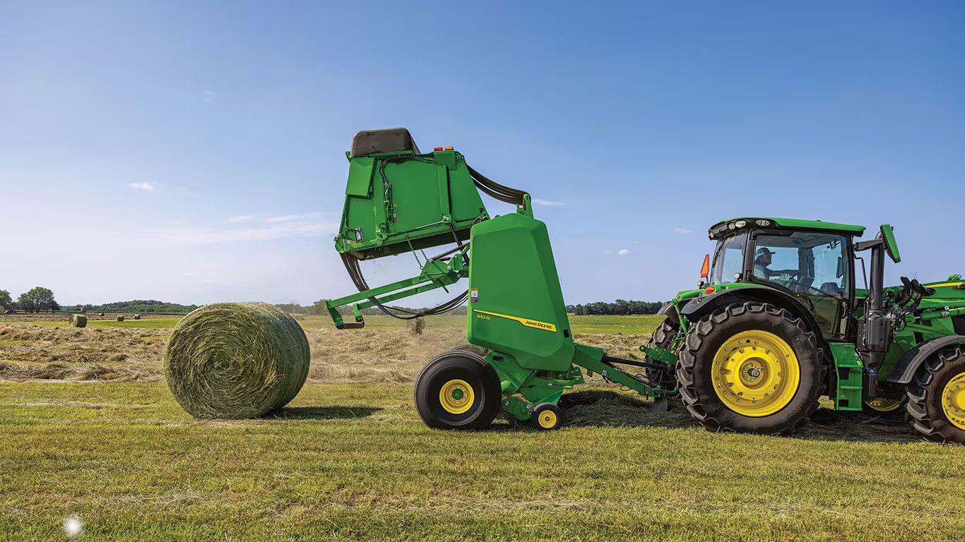 A John Deere Tractor and Hay Baler in the field ejecting a finished hay bale